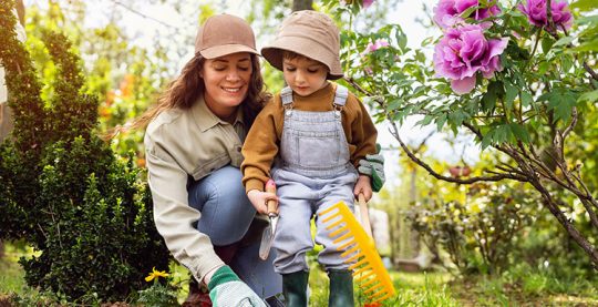 Adult and young child gardening outdoors wearing protective clothing: long sleeves, long pants, hats.