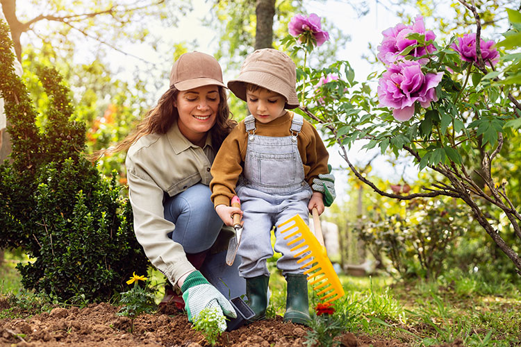 Adult and young child gardening outdoors wearing protective clothing: long sleeves, long pants, hats.